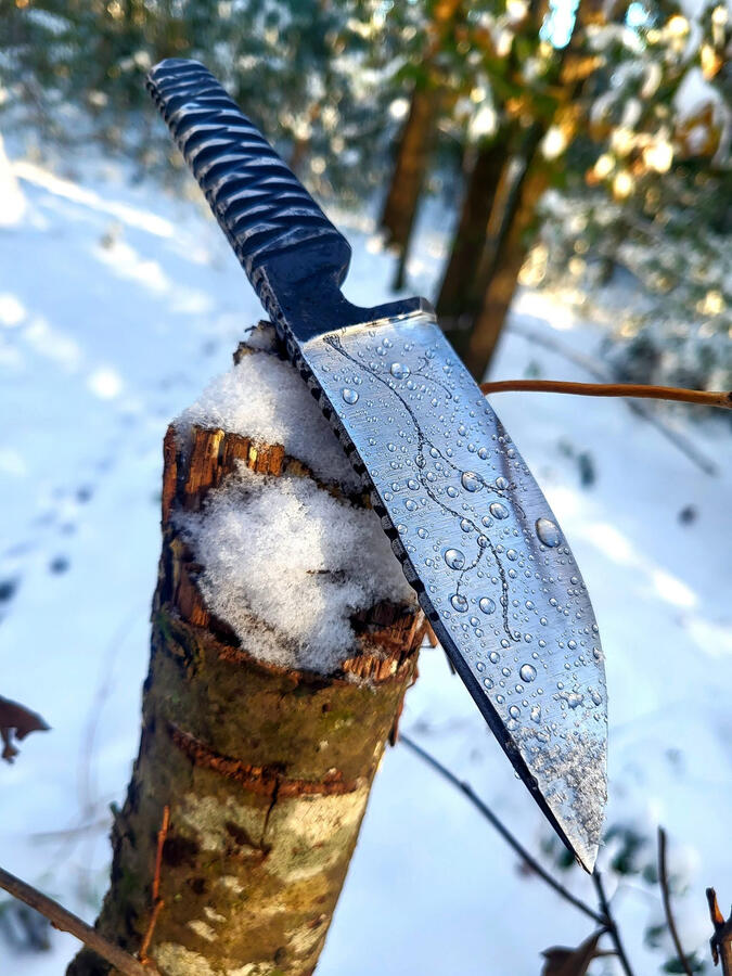 Hand forged knife on tree stump in snow